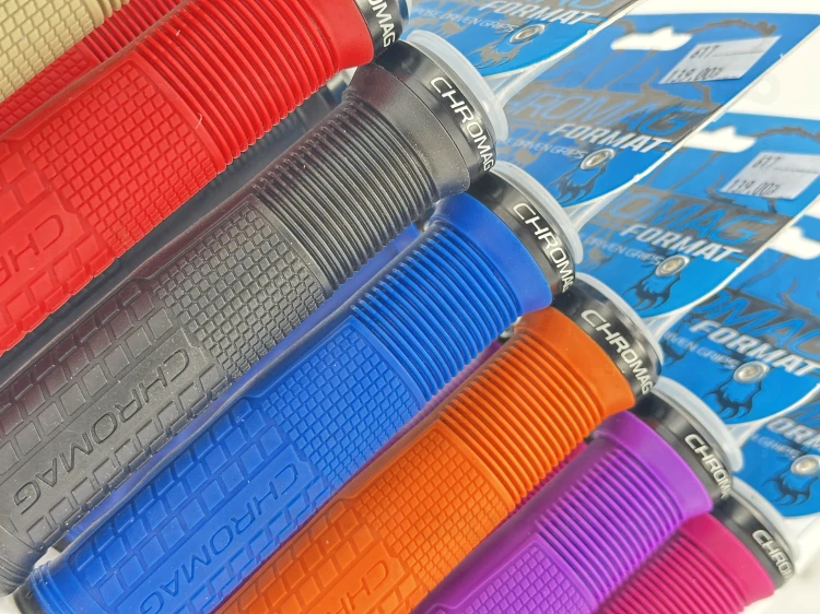 Gripy Chromag Format w kolorze piaskowym pomarańczowym, czarnym, niebieskim, różowym, fioletowym oraz czerwonym. Zbliżenie na bieżnik gripa oraz napis chromag.